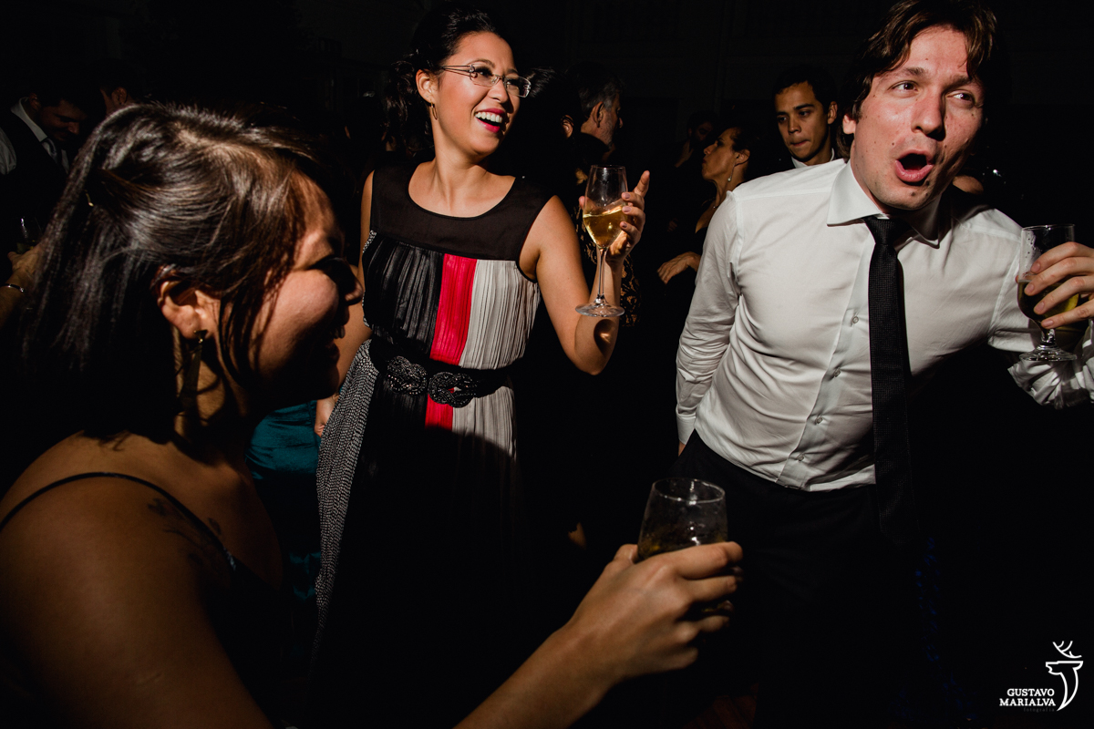 convidada cm taça de espumante na mão sorri enquanto convidado dança gritando e sorrindo