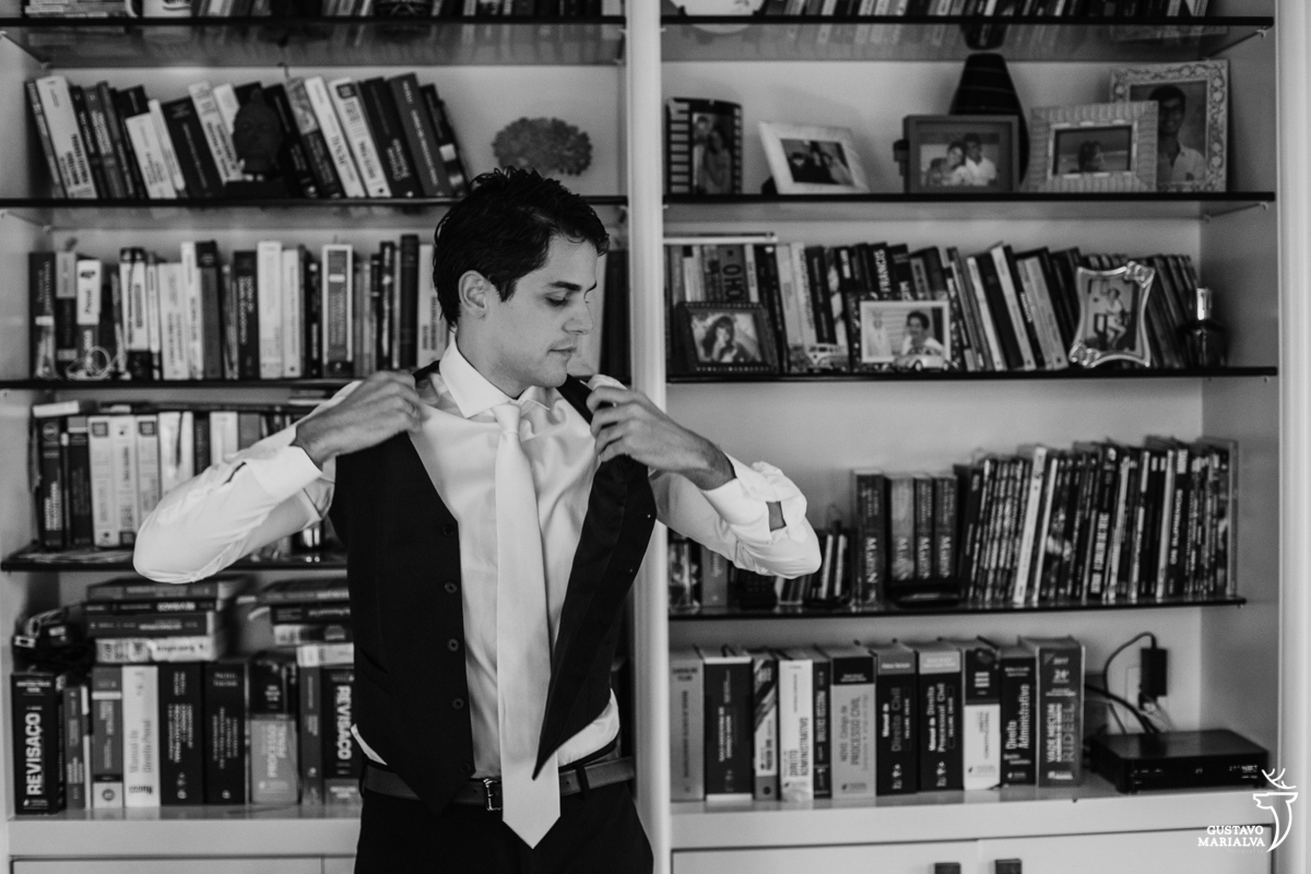 noivo colocando o colete com estante de livros ao fundo