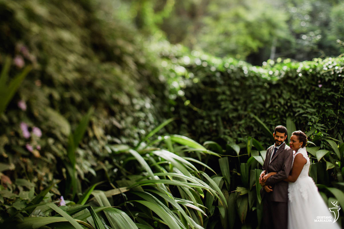noivos abraçados durante retrato de casamento em meio a parede de plantas verdes