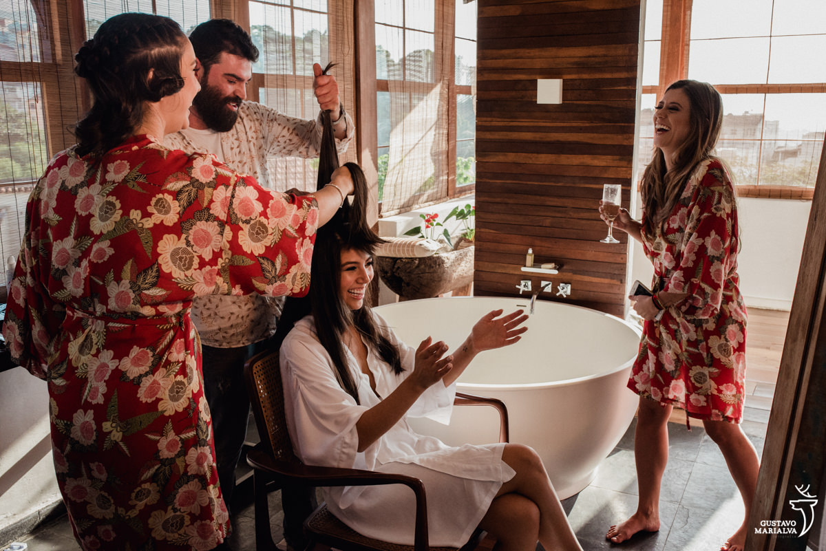 irmã da noiva segura o cabelo da noiva que sorri enquanto é observada pela madrinha sorrindo no making of do casamento no hotel santa teresa