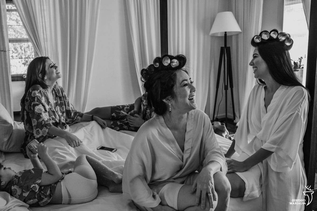 mãe sorri conversando com a noiva e madrinha ao fundo sorrindo durante o making of do casamento no hotel santa teresa