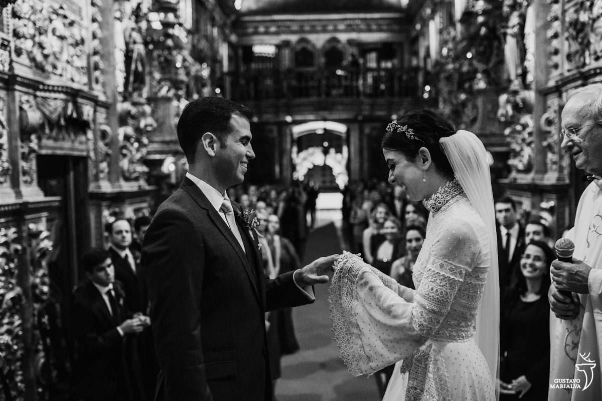 noiva coloca aliança no noivo e sorri durante a cerimônia de casamento