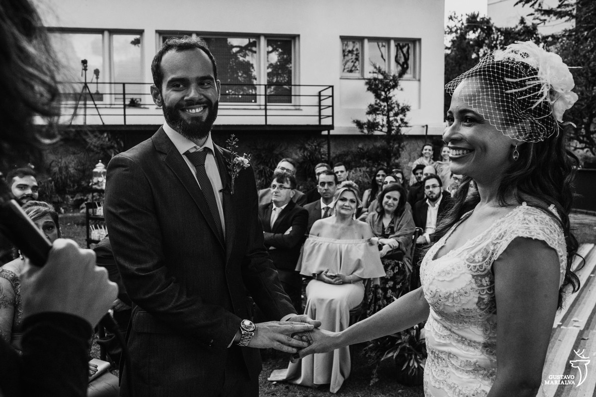 noivos sorrindo segurando as mãos sendo observados pelos convidados