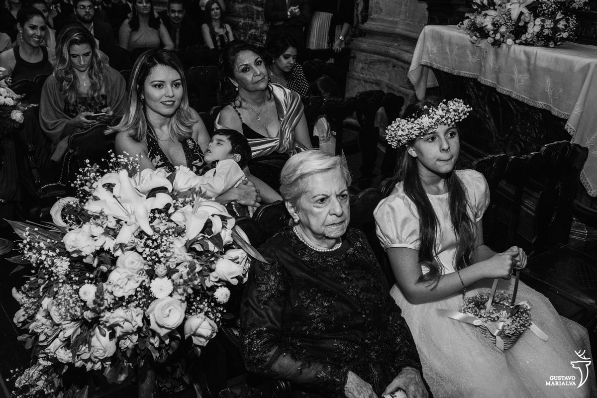 menino dorme no colo da mãe e senhora e daminha observam a cerimônia de casamento