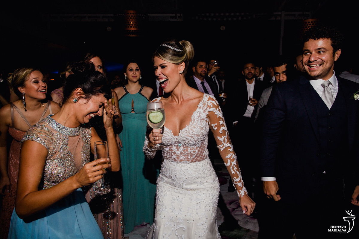 noiva sorri e dança com drink na mão enquanto madrinha coloca a mão no rosto