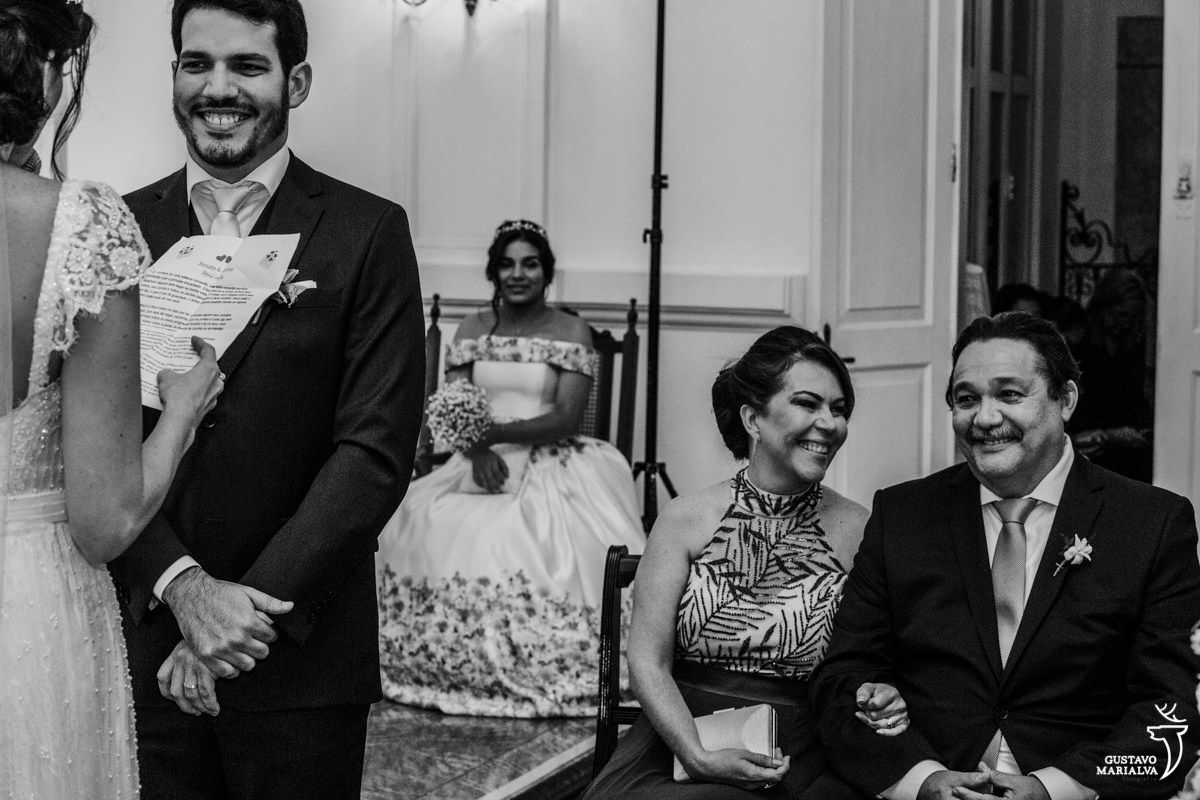 pais sorrindo emocionado e noivo sorrindo enquanto é observado pela daminha