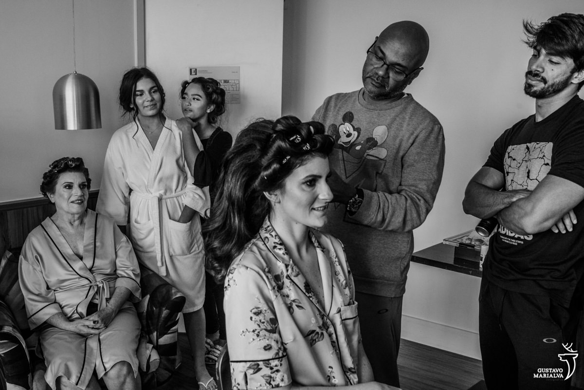 noiva arrumando o cabelo com maquiador usando um casaco do mickey sendo observada pela mãe e sobrinha usando um hobie branco