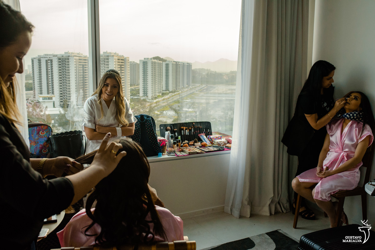 noiva ri e conversa com as amigas sentada no parapeito da janela com a barra da tijuca de fundo
