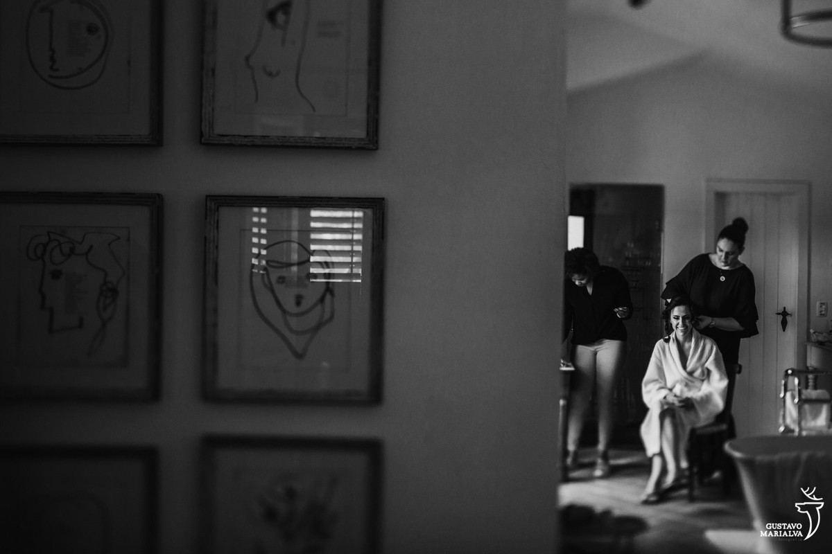 noiva sentada na cadeira se preparando para o casamento e uma série de quadros pendurados na parede do hotel vila da santa em búzios