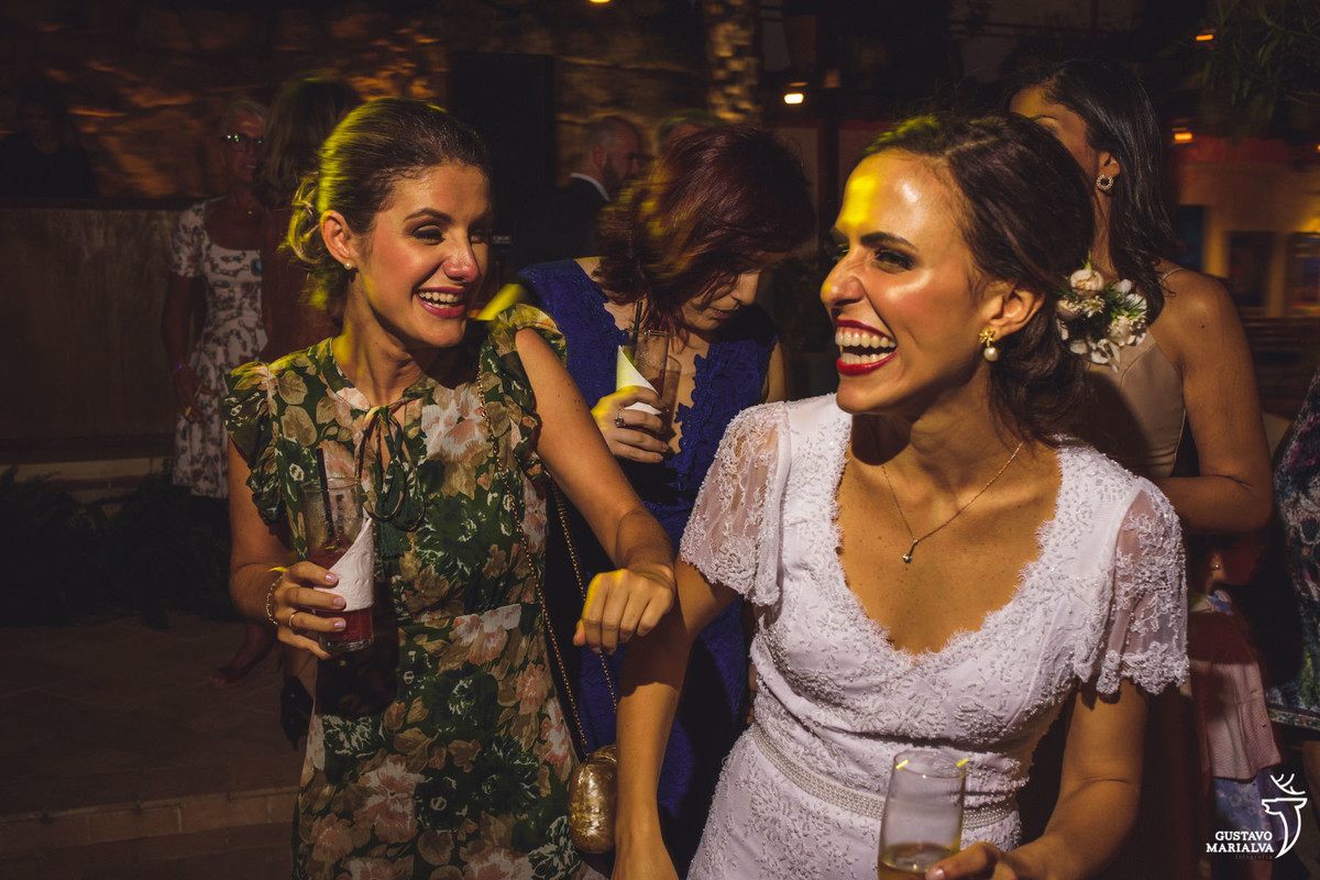 noiva dança com amiga segurando taça de espumante e sorrindo