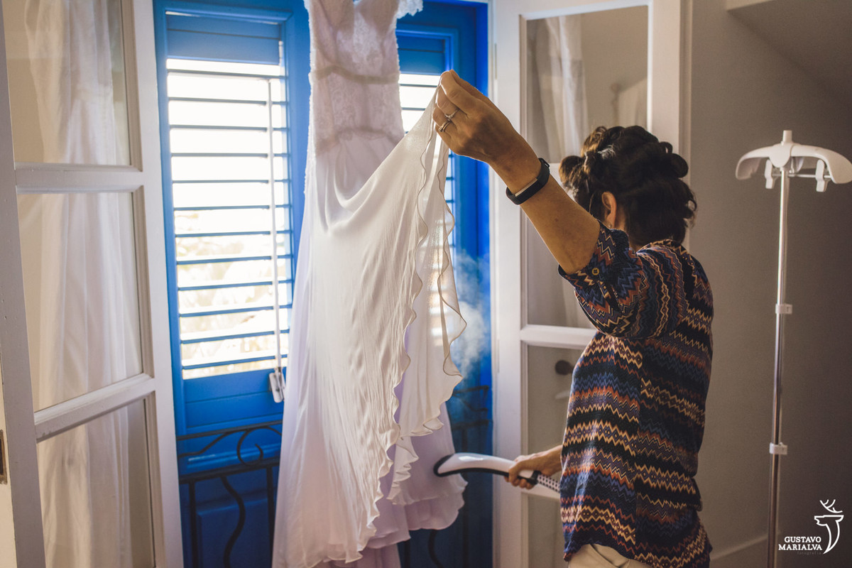 mãe da noiva passa o vestido de noiva pendurado na janela azul