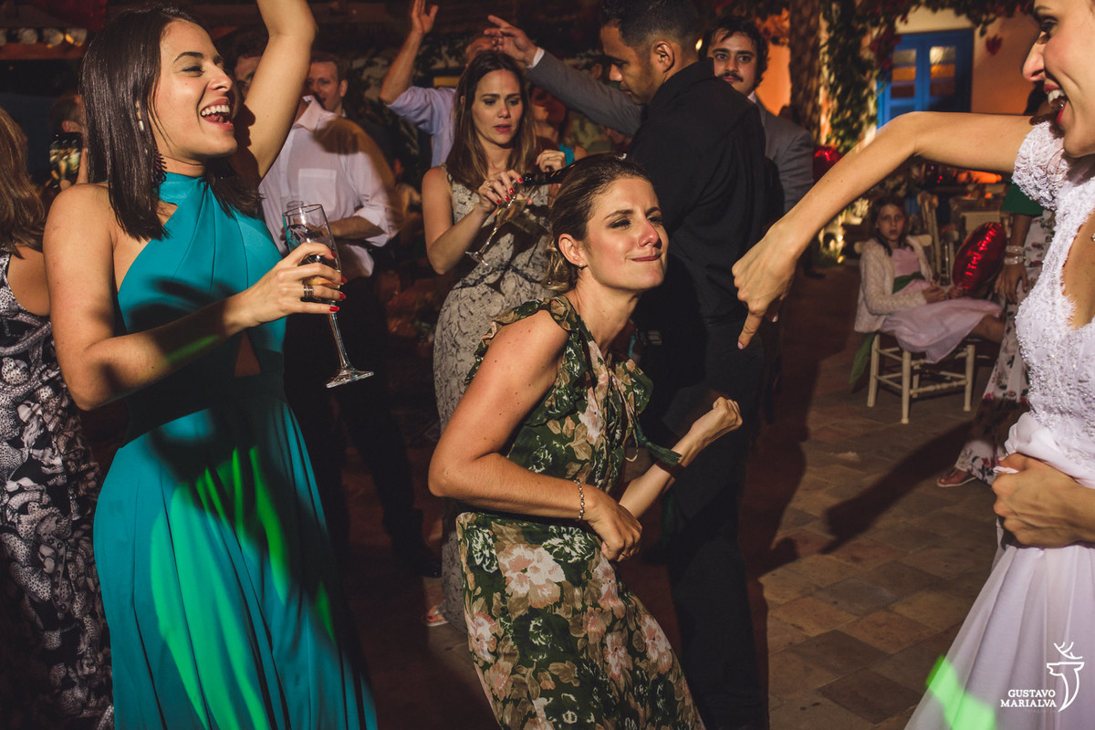 convidada faz air guitar e dança animada enquanto amiga pula com taça de espumante nas mãos