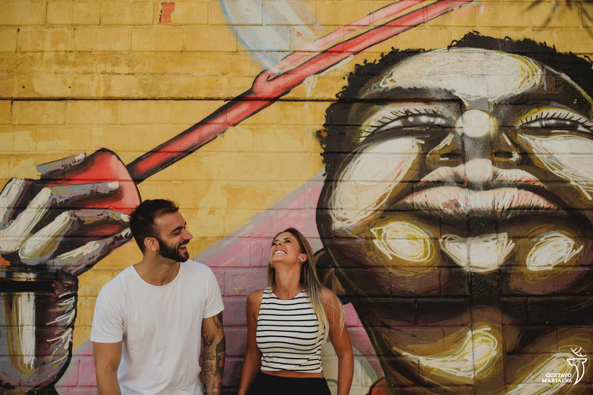 casal sorri olhando para cima com grafite desenhado na parede no largo da ordem em curitiba