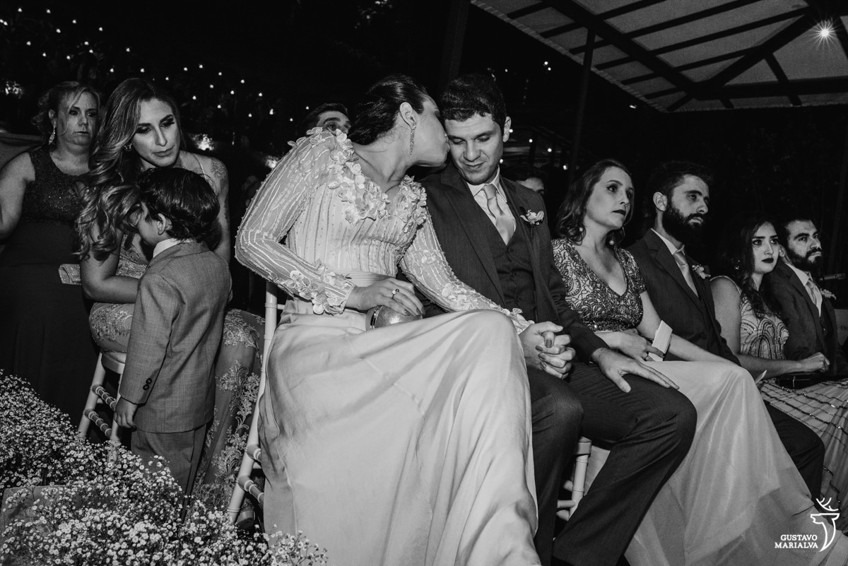 casal se beija de mãos dadas durante a cerimônia de casamento e menino brinca ao fundo