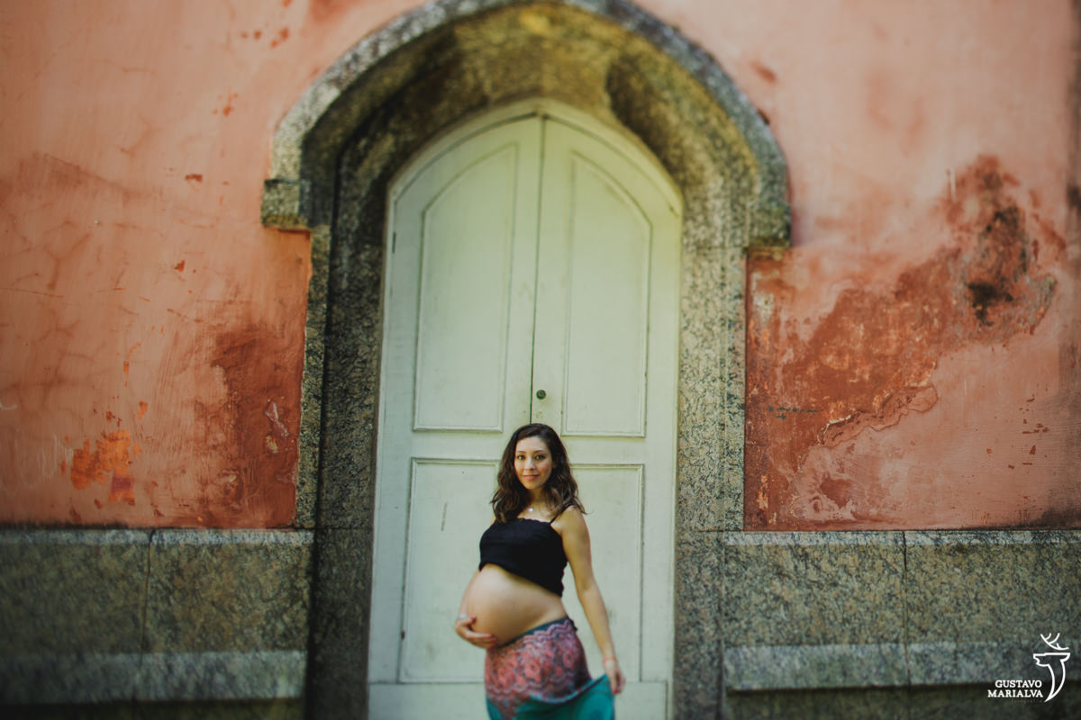 mulher grávida faz carinho na barriga e segura a saia em frente a porta branca no parque lage