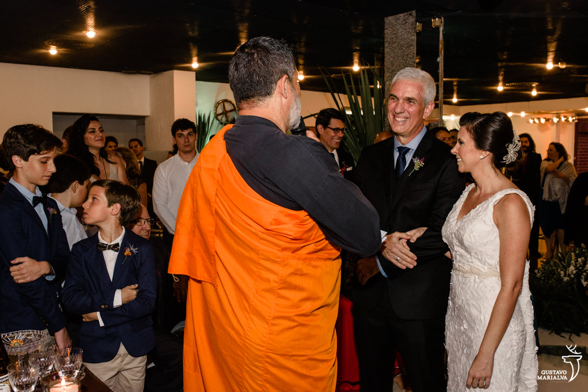 noivos sorridentes escutam o monge budista durante a cerimônia do casamento