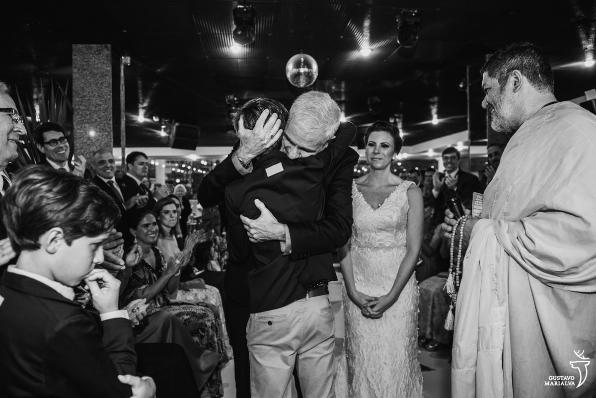 pai abraça o filho emocionado e é observado pela noiva que chora durante a cerimônia de casamento