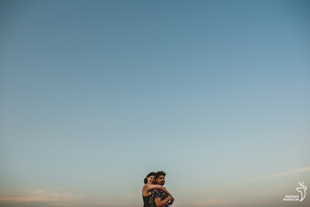 esposa abraça o marido por trás com o por de sol ao fundo