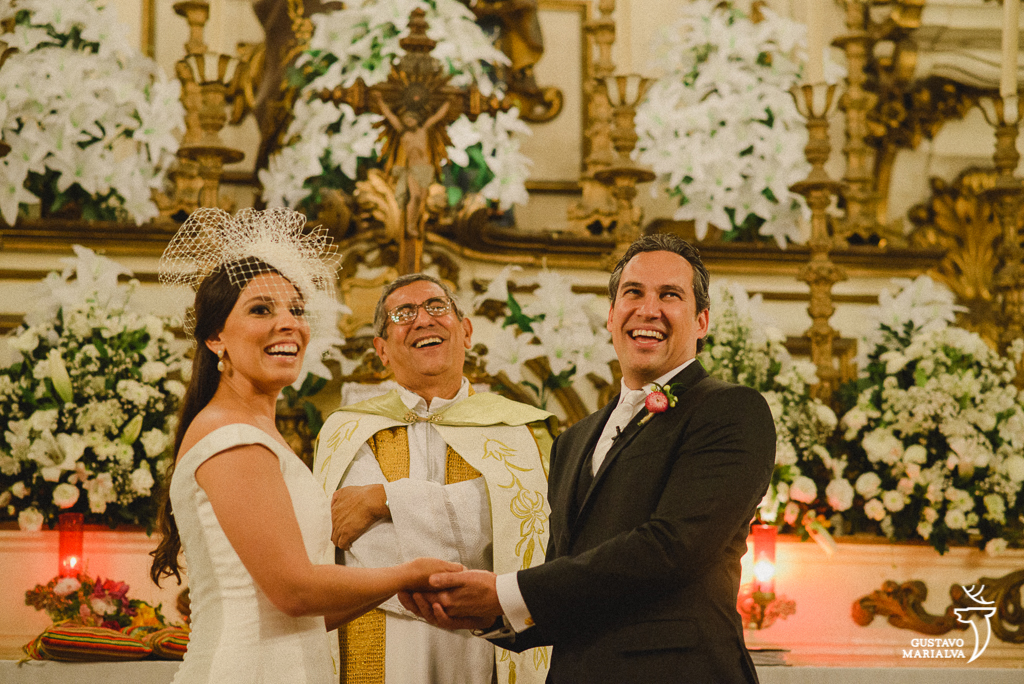 noivos e padre sorrindo na cerimônia de casamento