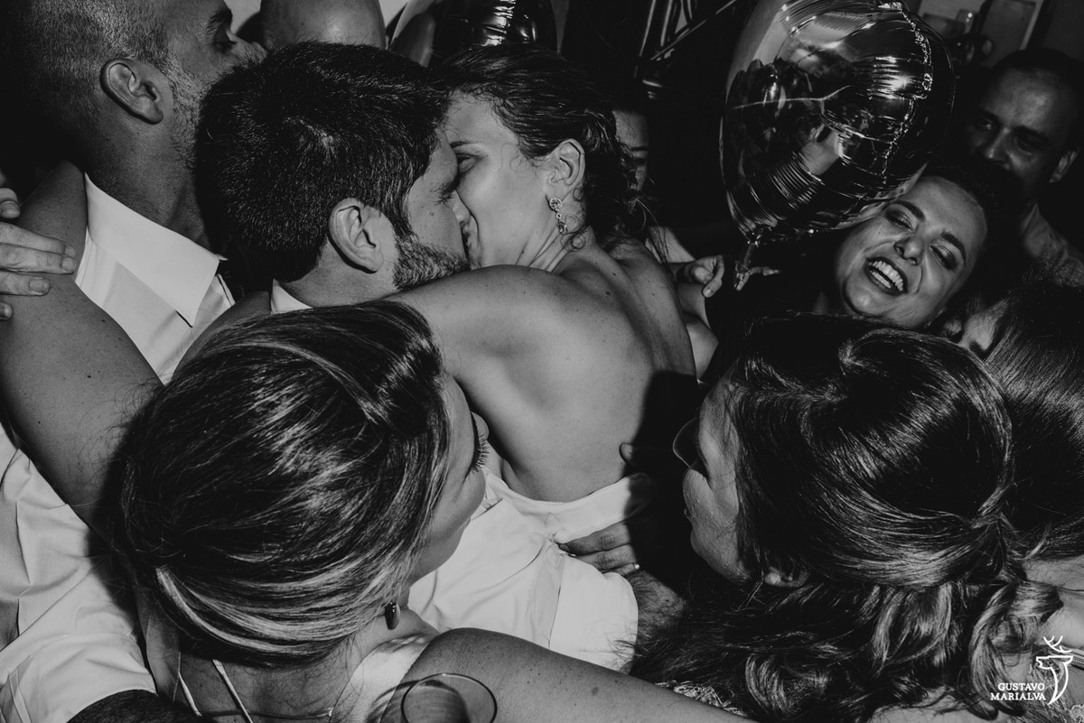 noivos se beijando e sendo abraçados pelos convidados na festa de casamento