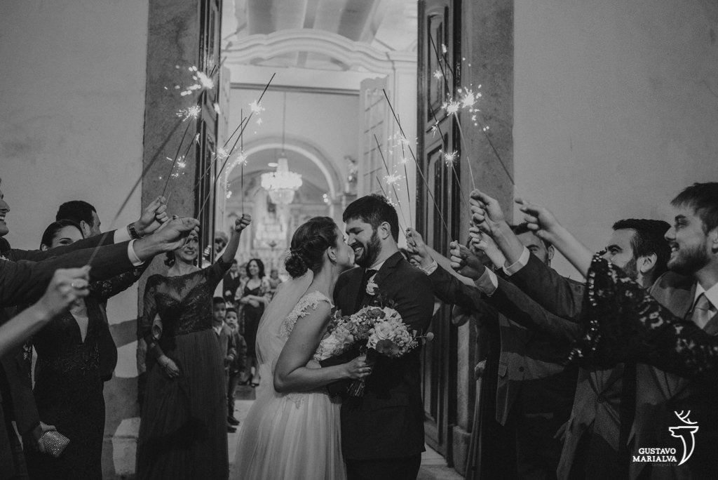noivos se beijando na saída da cerimônia de casamento com os padrinhos segurando sparkles