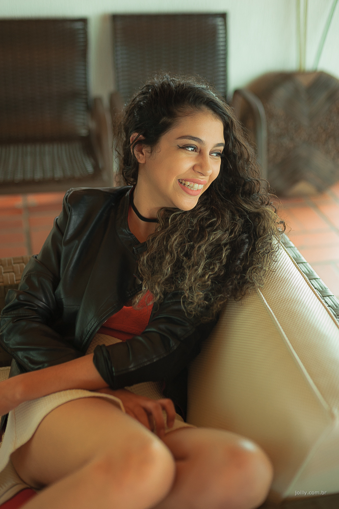 lindo sorriso dessa moça estilosa com jaqueta de couro preta sentada no sofá