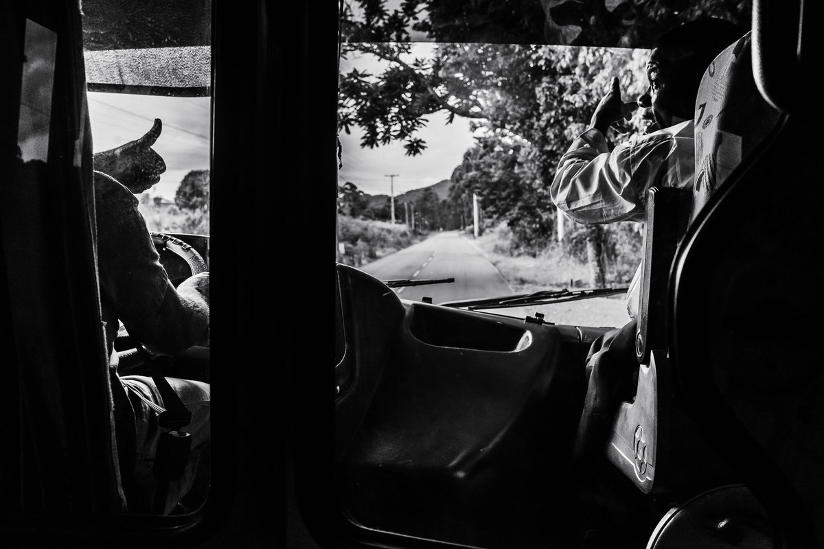 Dentro do ônibus está o motorista que acena com o polegar em direção ao passageiro sentado à sua direita que confirma o caminho a ser seguido