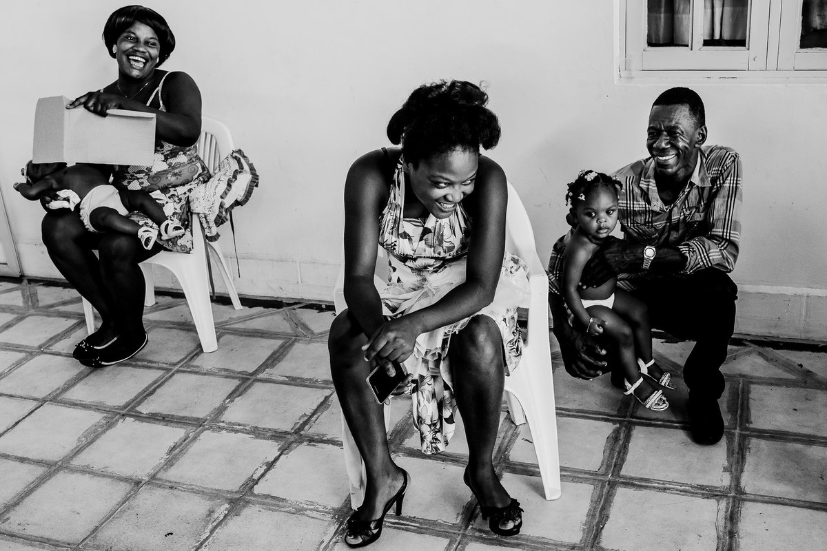 During the hatian wedding the smiling guests spontaneously sit with their babies on their laps making wind with piece of paper to refresh while it is warm