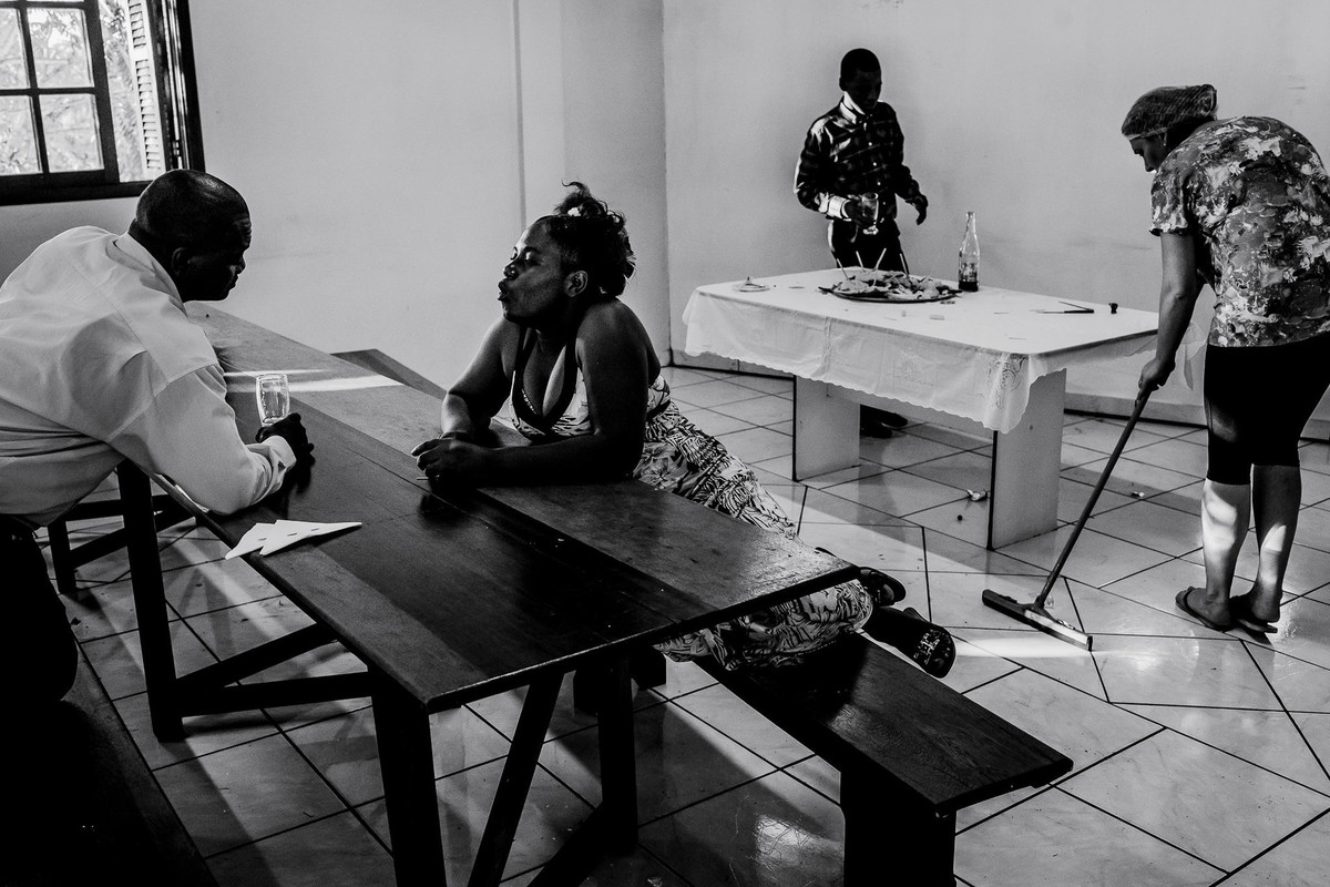 A couple are exchanging looks at a table while a woman behind them is cleaning the floor of the party room and a child is watching the candy table that is almost empty