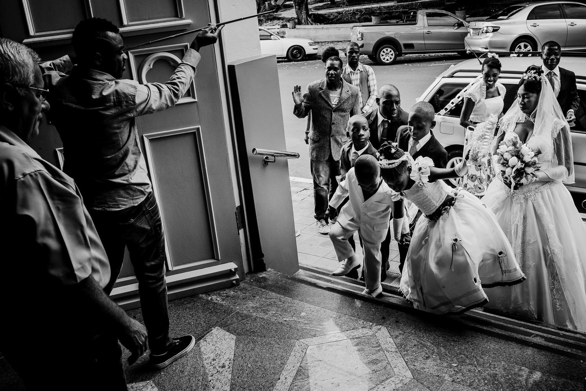 Os pajens e a daminha de honra sobem a escadaria da igreja de Estrela enquanto a noiva está atrás deles ao lado de amigos, tem alguém com pau de selfie dentro da igreja filmando a entrada