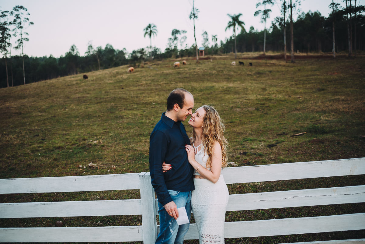 casal troca carinho ao ser fotografado no campo junto às ovelhas
