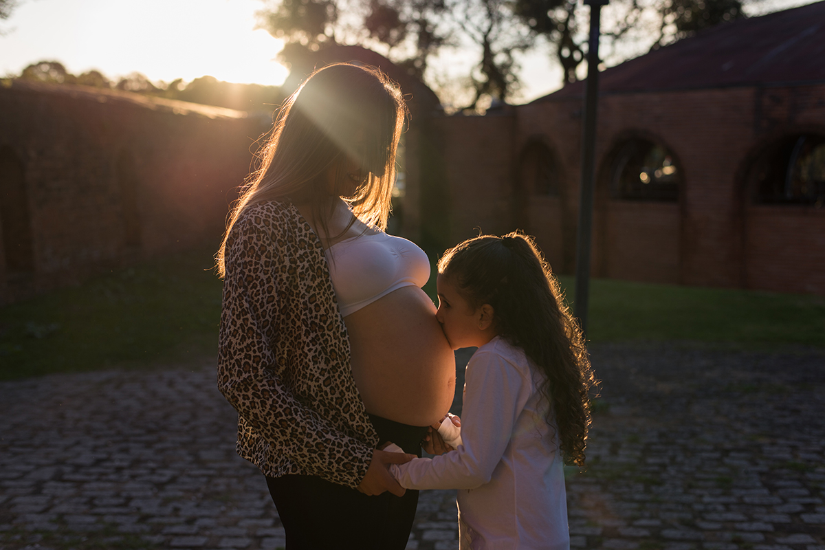 grávida gestante mamãe vestido azul cinto pérolas parque árvore dia sol beijo barriga