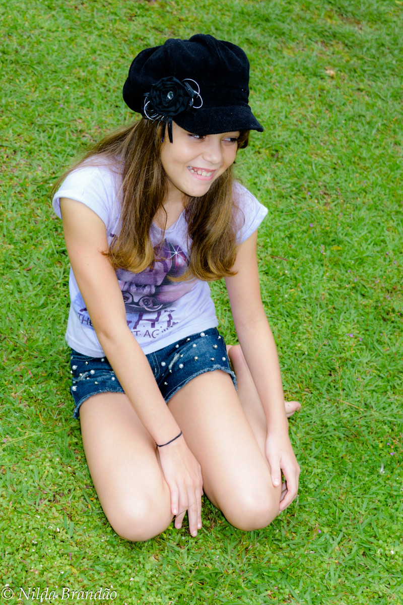 Menina sentada na grama, usando short jeans e camiseta