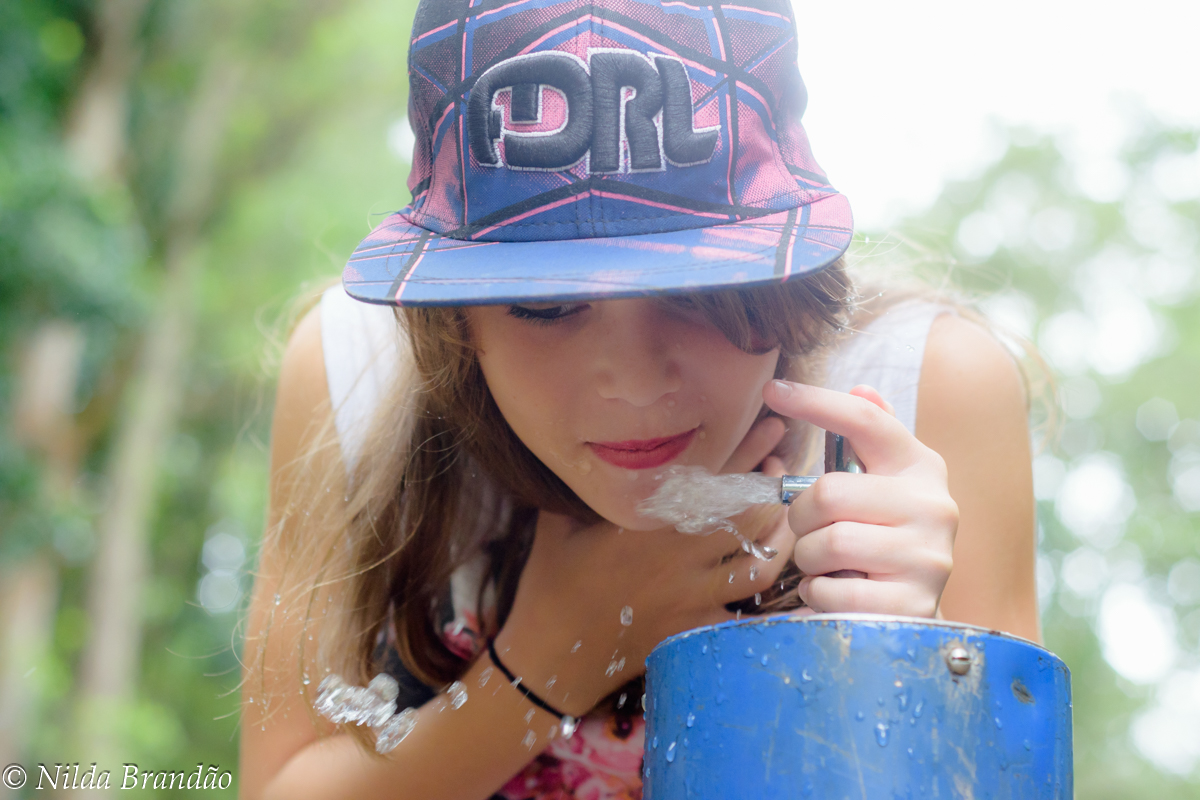 Menina bebendo agua em fonte no parque