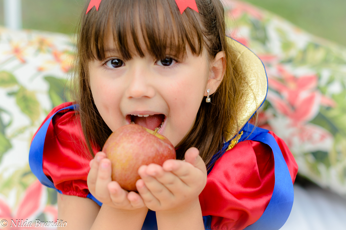 Menina com fantasia de branca de neve dando primeira mordida na maçã