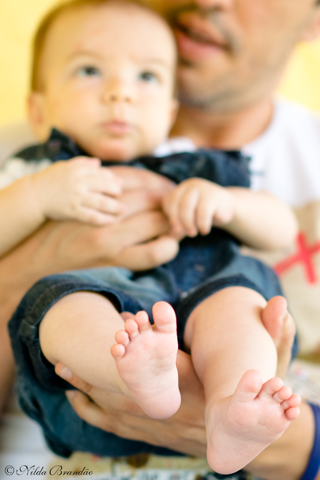 Pezinhos em destaque na foto que o papai segura o bebê no colo.
