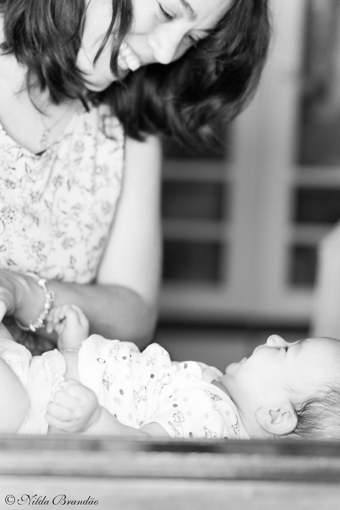 Fotografia em preto e branco mostra mamãe sorrindo para o bebê enquanto troca sua frauda.