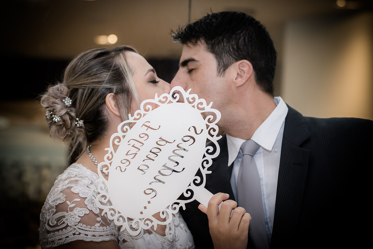 Noiva se esconde atras de placa de "felizes para sempre" para beijo em frente a mesa do bolo.