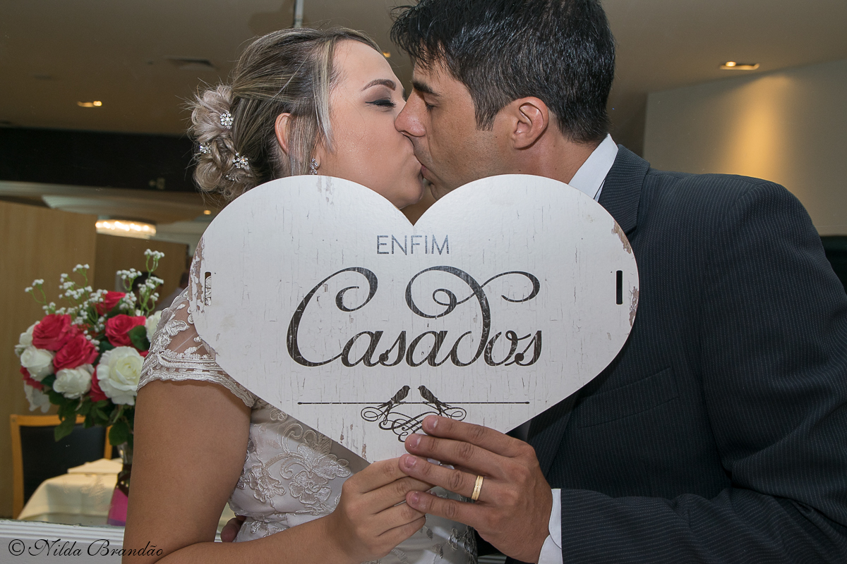 Enfim, casados! diz a placa que os noivos seguram enquanto se beijam
