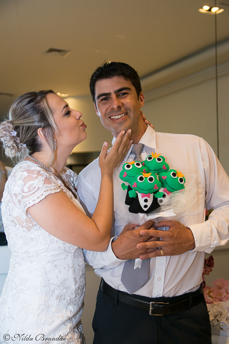 Noivo segura o buquê de sapinhos no mini wedding, enquanto noiva tenta beija-lo.