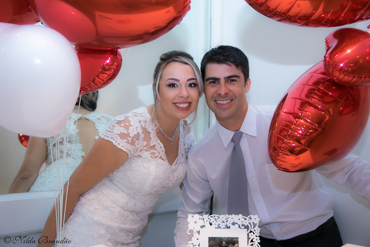Casal posa para fotografia junto aos balões de coração