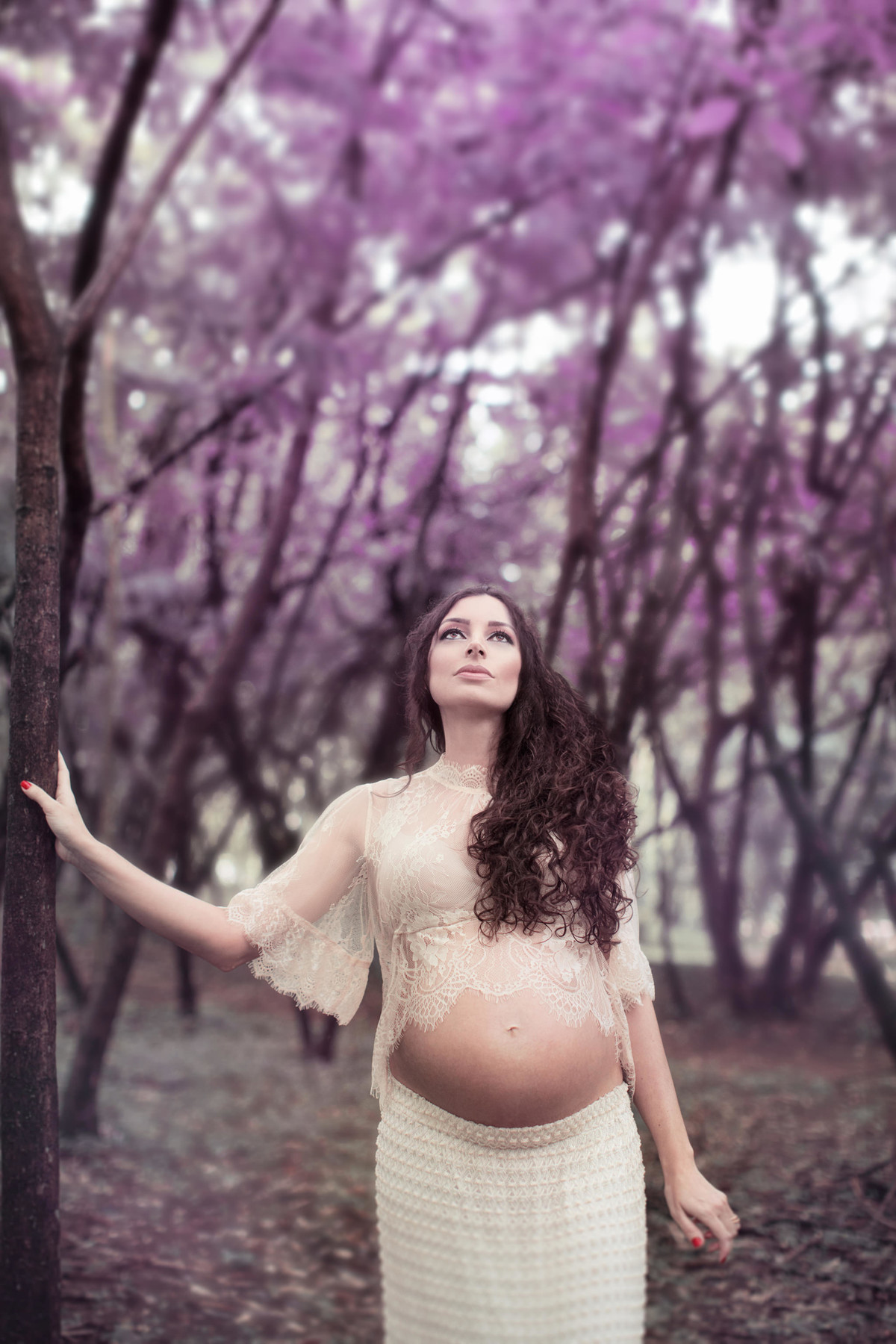 Grávida apoiada na arvore em floresta cor de rosa. Fotografada pelo fotógrafo de gestante Rafael Ohana em Brasília-DF.