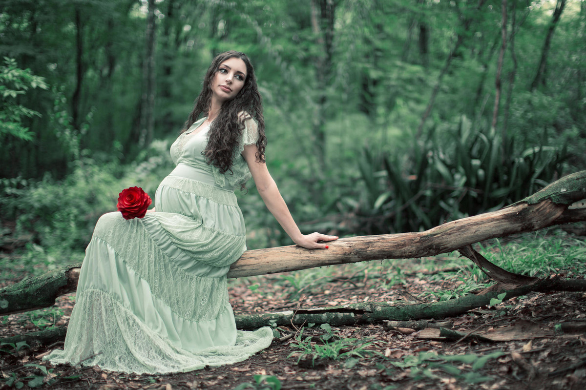 Grávida sentada em tronco de arvore segurando flor vermelha. Fotografada pelo fotógrafo de gestante Rafael Ohana em Brasília-DF.