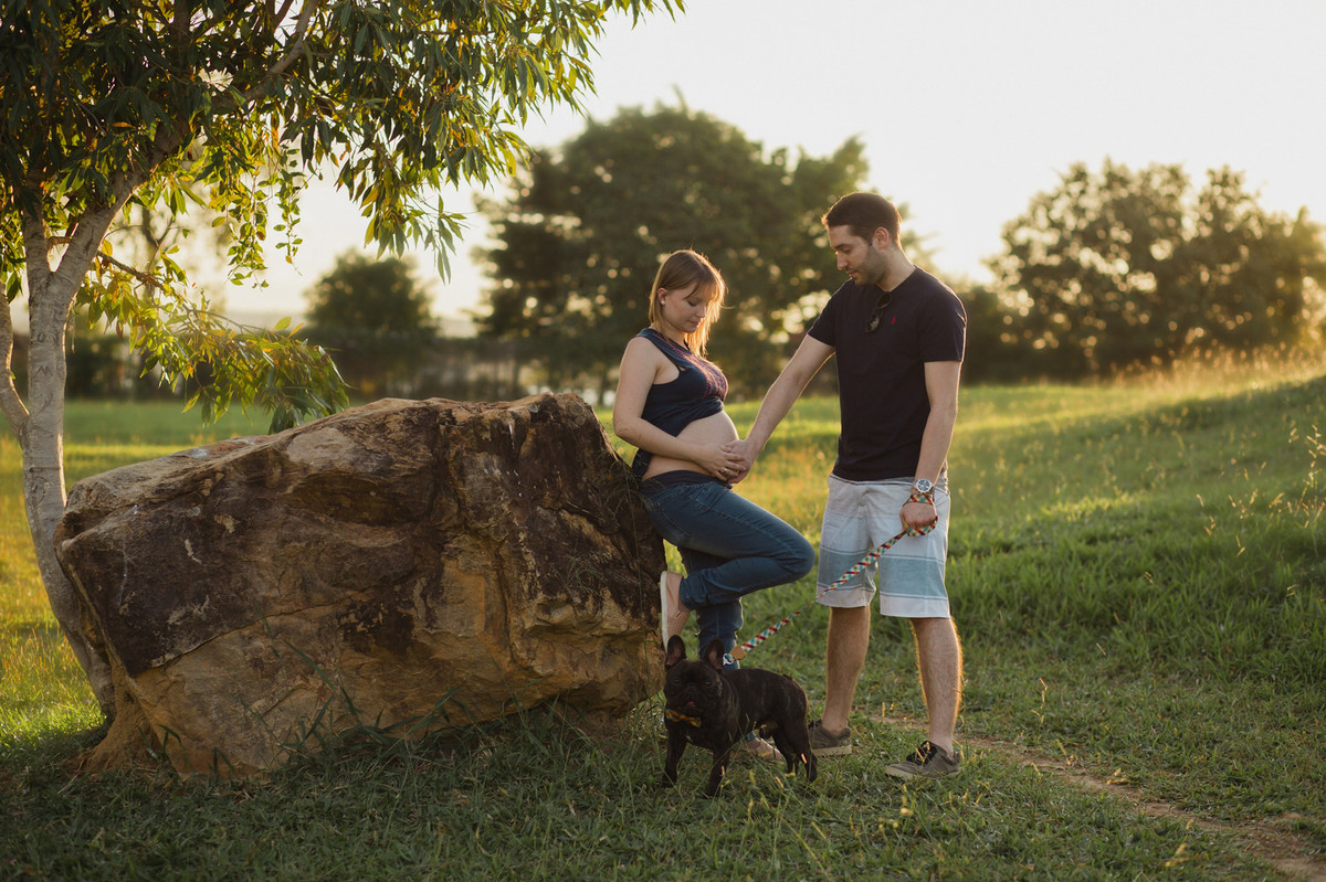 Ensaio de família feito no Lago Norte. Grávida apoiada em pedra com cachorro.