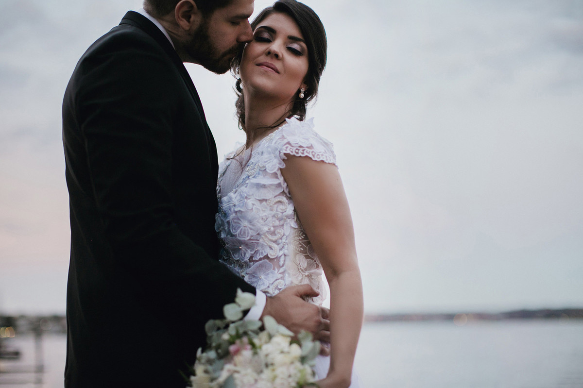 Noivo beijando bochecha da noiva perto do lago