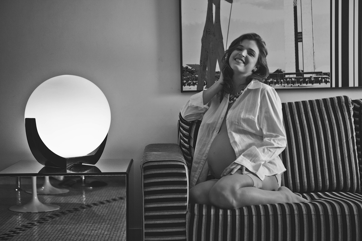 Milena grávida sentada no sofá listrado ensaio feito em Brasília DF
