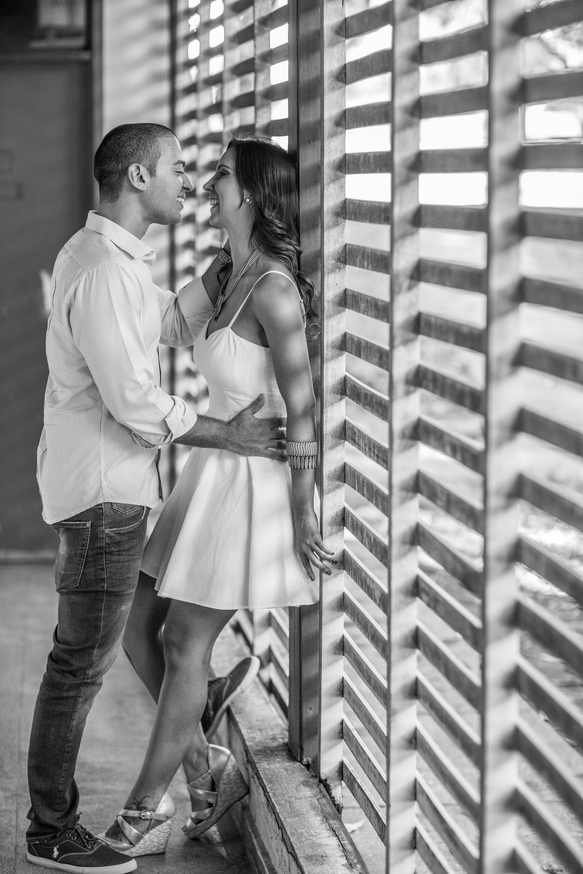 Casal sorrindo abraçados perto de janela de madeira. Foto feita pelo fotógrafo de casamento Rafael Ohana em Brasília-DF