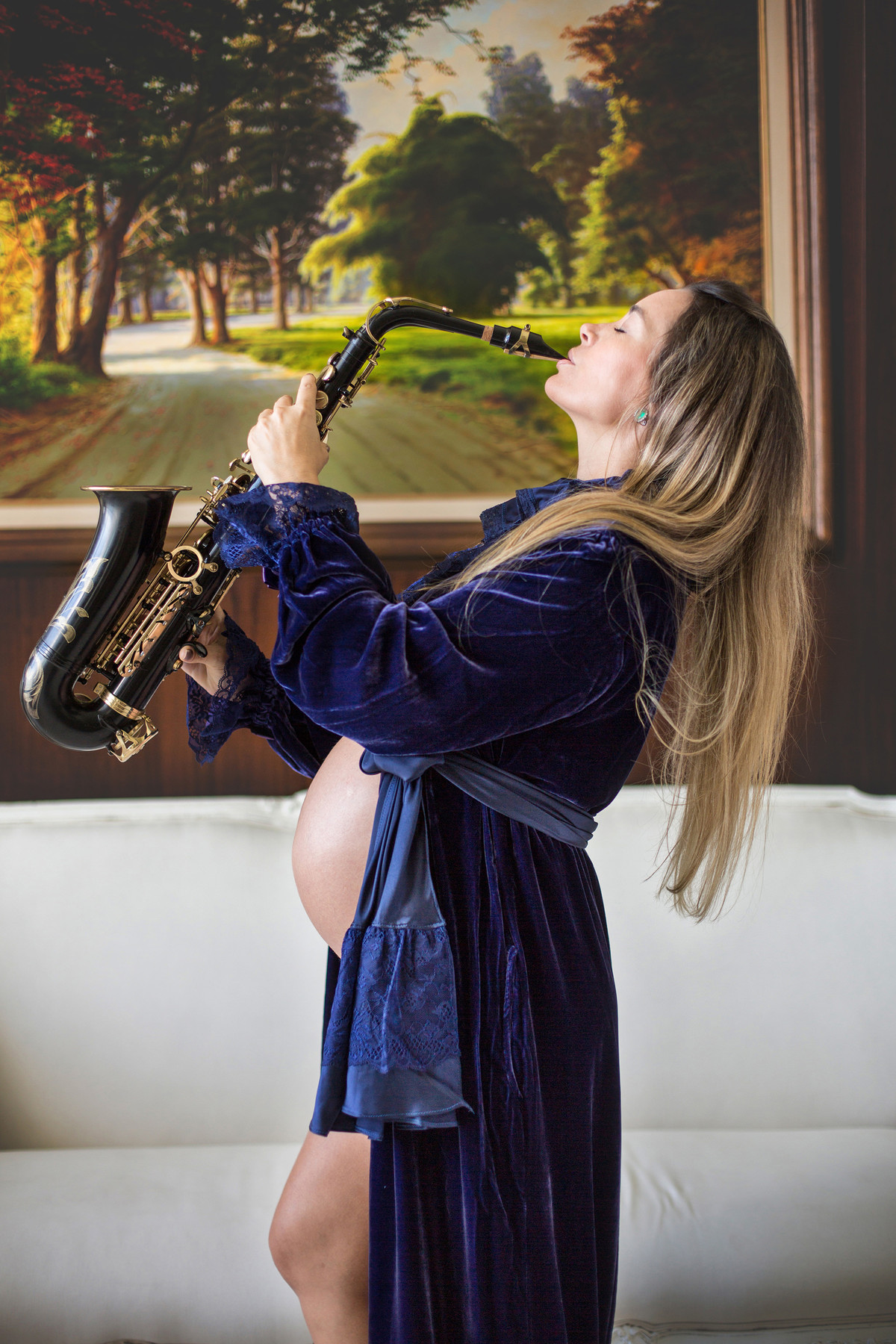 Grávida tocando saxofone usando vestido azul de veludo. Ensaio fotografado pelo fotógrafo de gestantes Rafael Ohana em Manaus-AM.