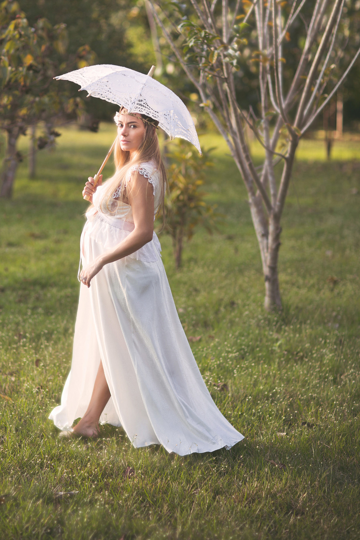 Grávida passeando pelo campo de vestido branco e sombrinha branca de renda. Fotografado pelo fotógrafo de gestantes Rafael Ohana em Manaus-AM