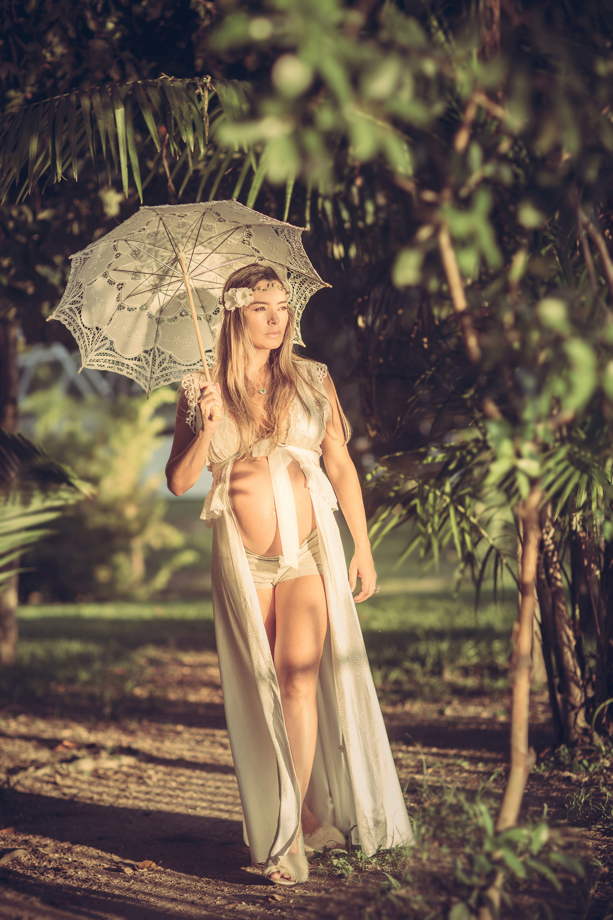 Grávida passeando pela floresta usando vestido branco e uma sombrinha branca de renda. Fotografado pelo fotógrafo de gestantes Rafael Ohana em Manaus-AM